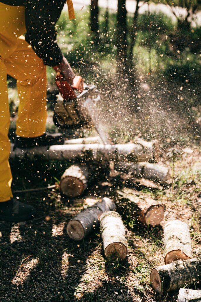 Faceless worker using chainsaw to cut logs with sawdust flying in a forest setting.